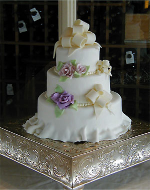 three layer cake with ruffles and bows and purple roses