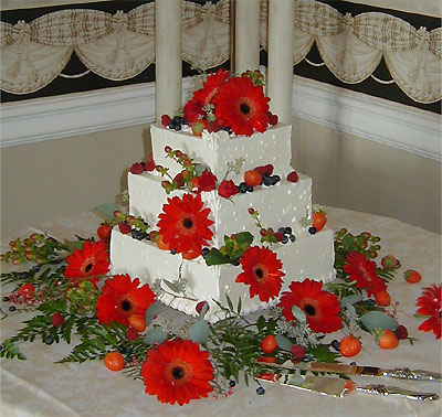 Three layer square cake with red daisies and berries
